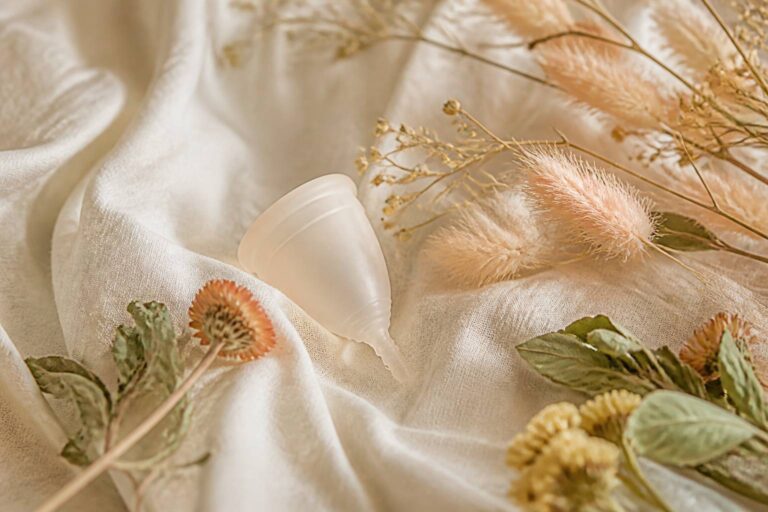 Menstrual cup silicone on soft white fabric with dried flowers, natural light wellness ambiance