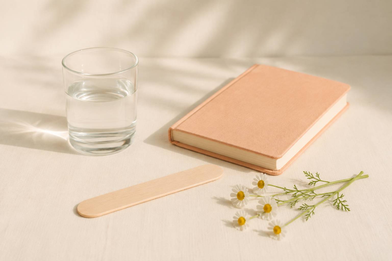 Glass of water, wooden tongue depressor and chamomile sprig arranged on a cream background